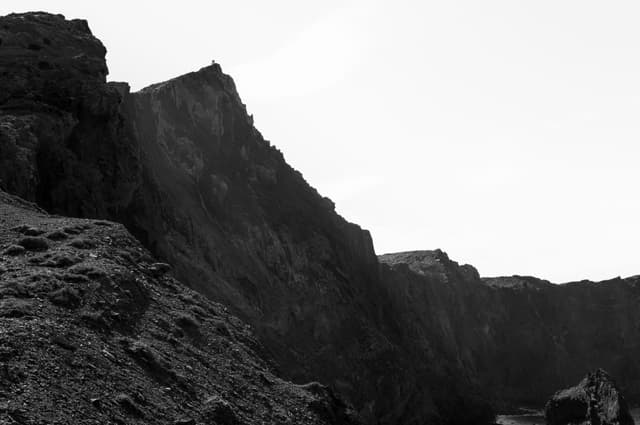 Black and white photograph of steep rocky cliffs against an open sky, with rough textured rocks in the foreground