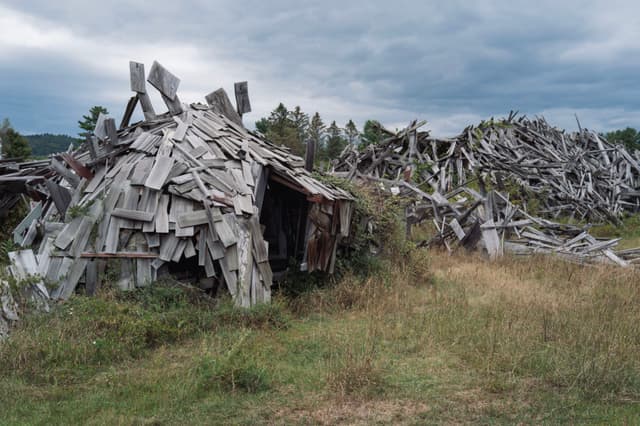 Deteriorated wooden structures scattered across a grassy landscape under a cloudy sky