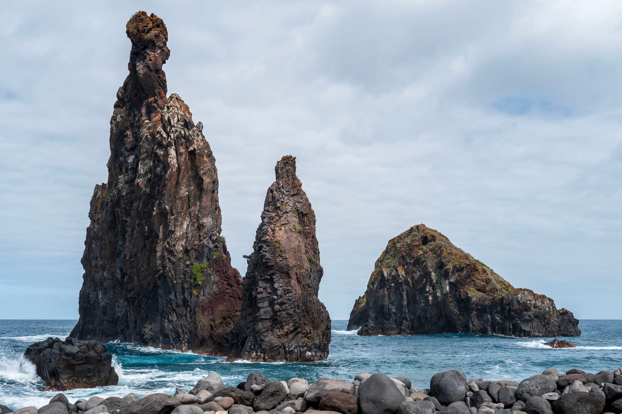 Three dramatic sea stacks against a cloudy sky, surrounded by ocean waves and rocky shore