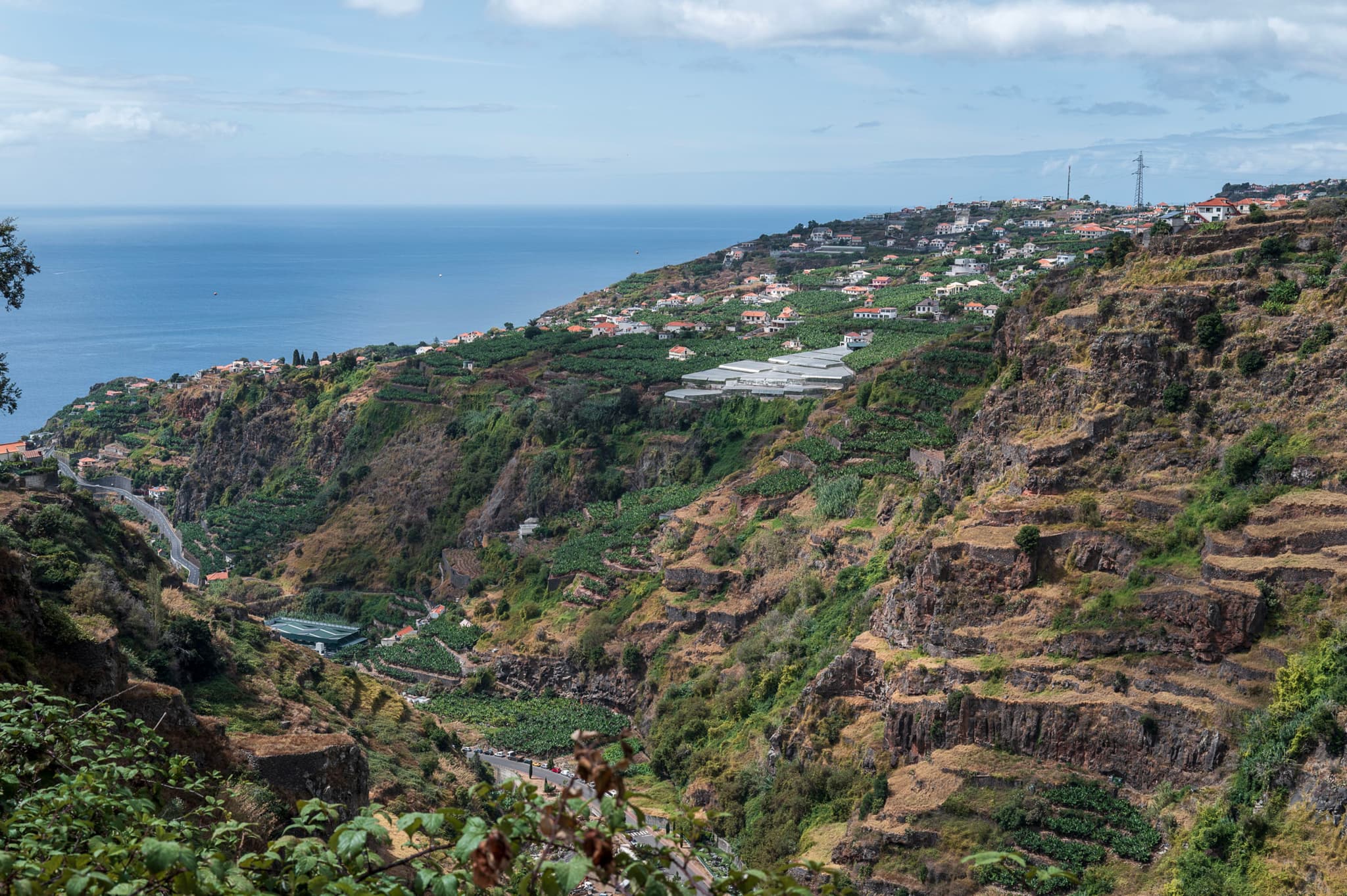 Terraced hills overlooking the ocean, with patches of greenery and a distant coastline under a partly cloudy sky