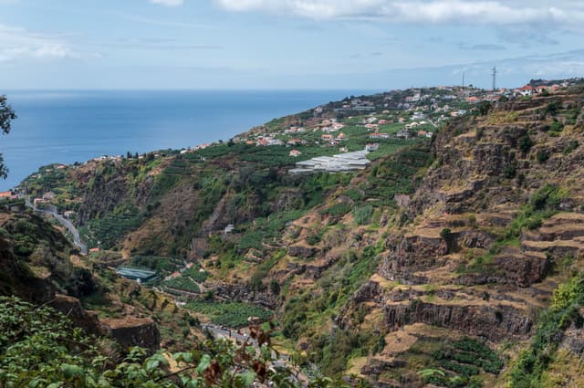 Terraced hills overlooking the ocean, with patches of greenery and a distant coastline under a partly cloudy sky