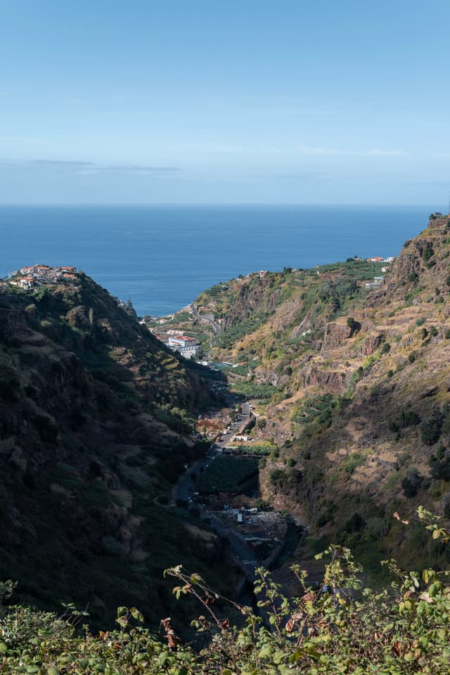 A lush valley with mountains on either side leading to the ocean under a clear blue sky
