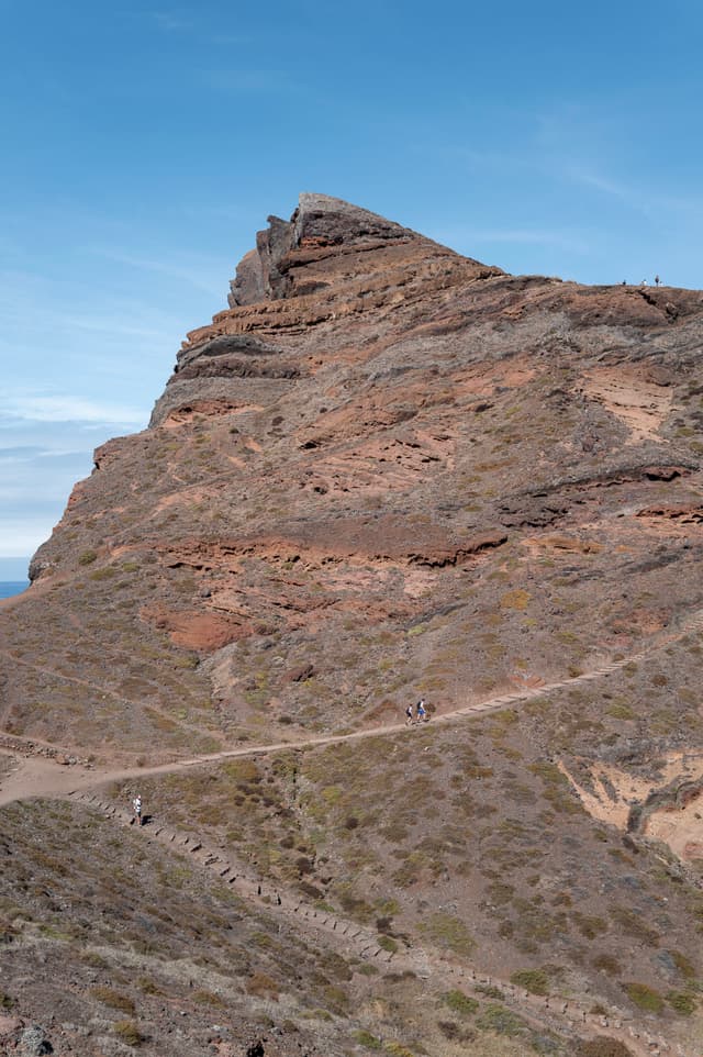 A rugged mountain peak with a winding path under a clear blue sky