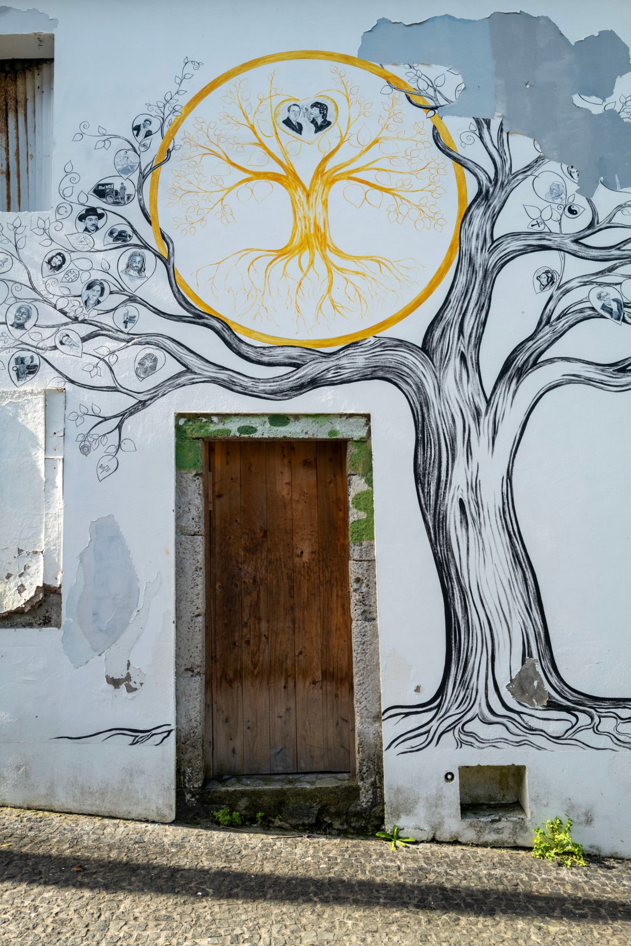 A mural on a wall features a large tree with intricate branches and roots, surrounding a wooden door. The tree's roots form a circular design with a heart shape at the center