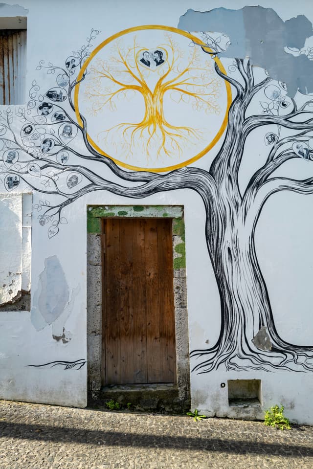 A mural on a wall features a large tree with intricate branches and roots, surrounding a wooden door. The tree's roots form a circular design with a heart shape at the center