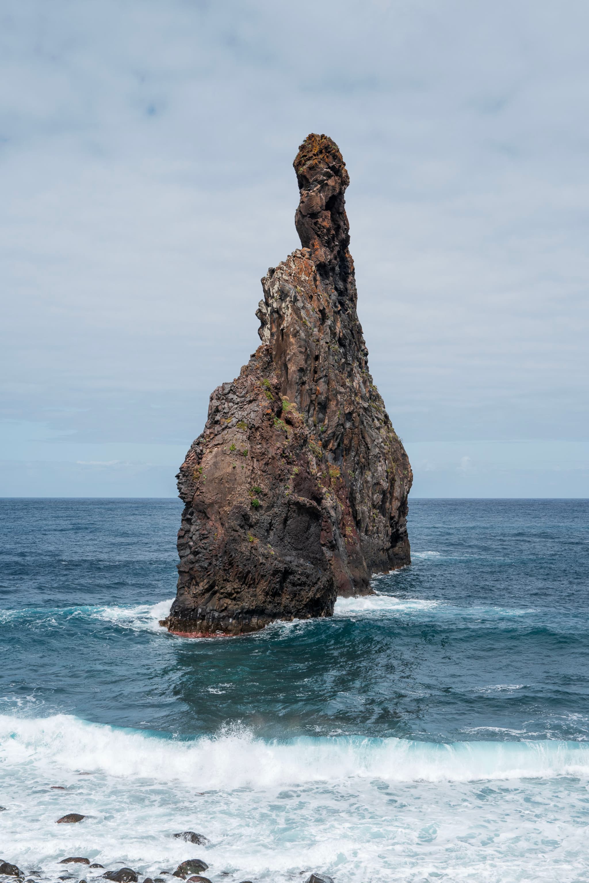 A solitary towering rock formation rising from the ocean waves under a cloudy sky