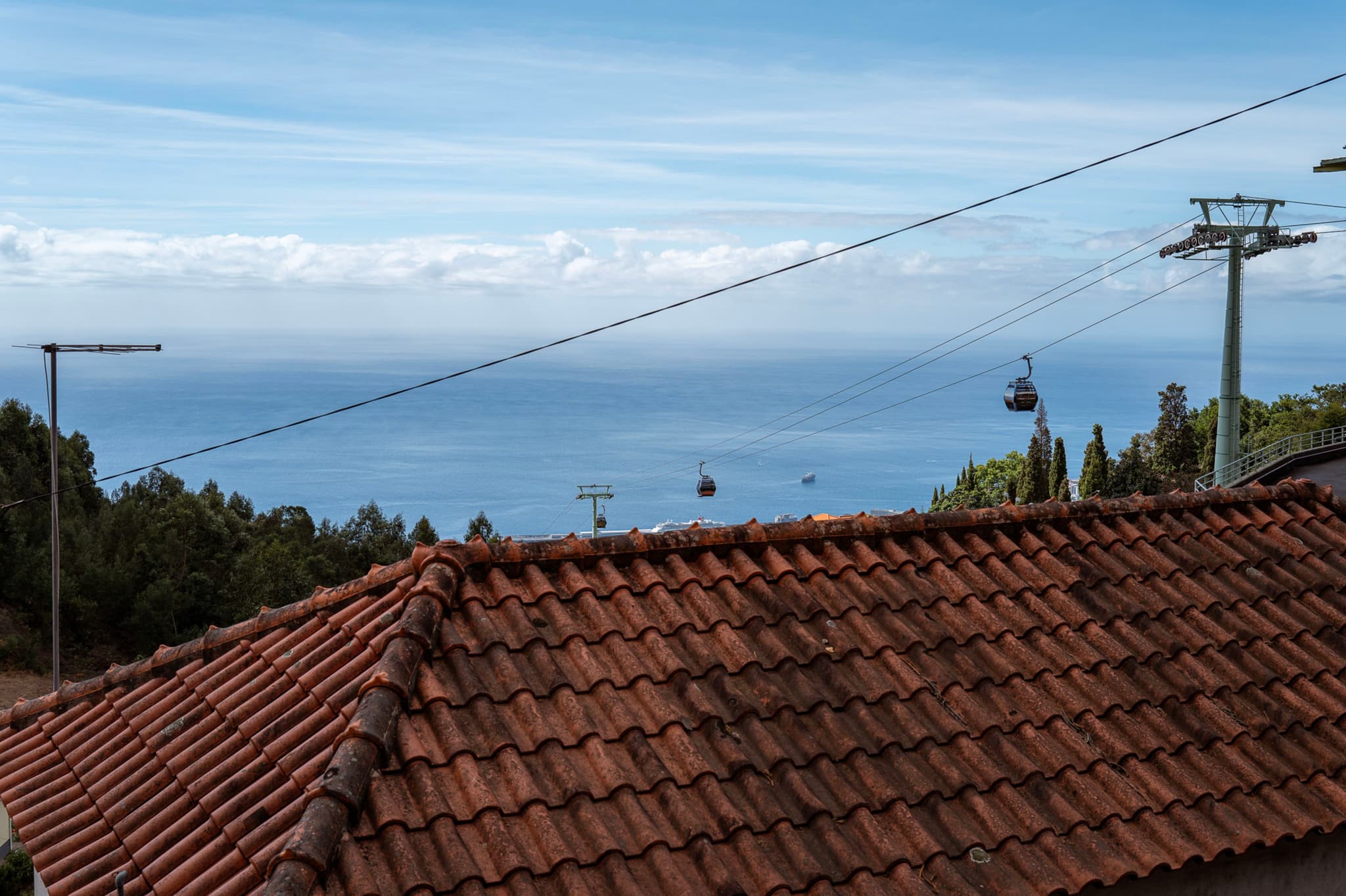 A rooftop with cable cars in the distance, overlooking a vast ocean under a partly cloudy sky