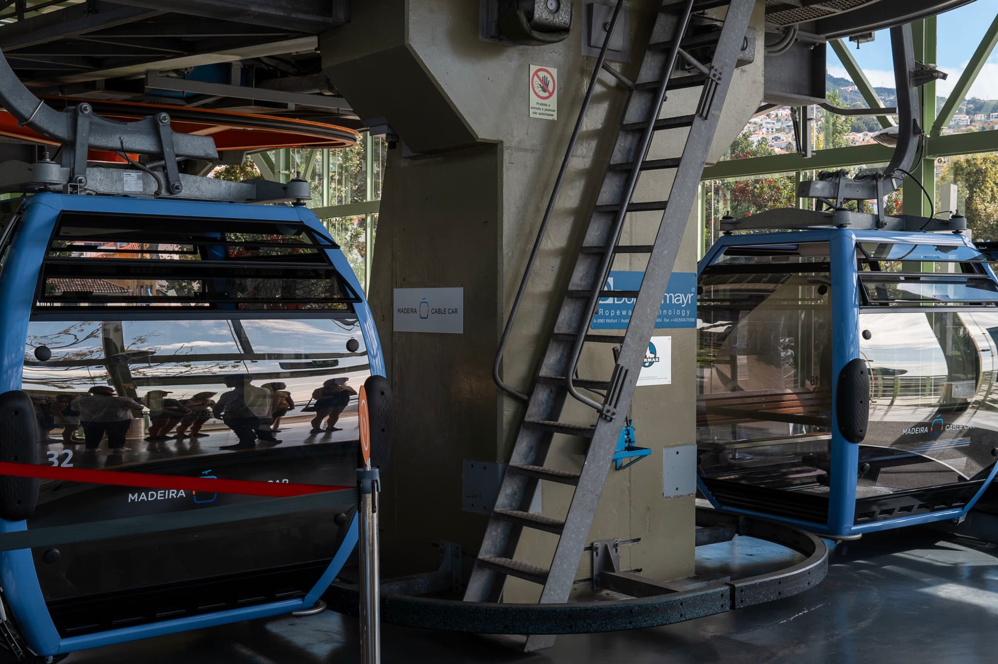 Two blue gondola cable cars at a station with reflections on their glass