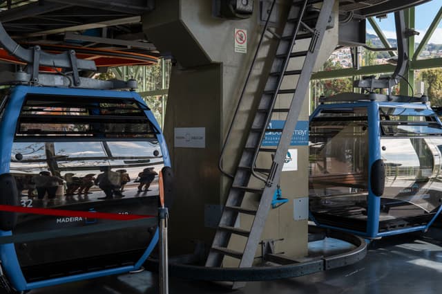 Two blue gondola cable cars at a station with reflections on their glass