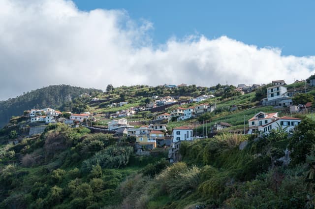 A hillside village with white houses and terracotta roofs nestled in lush greenery beneath a partly cloudy sky