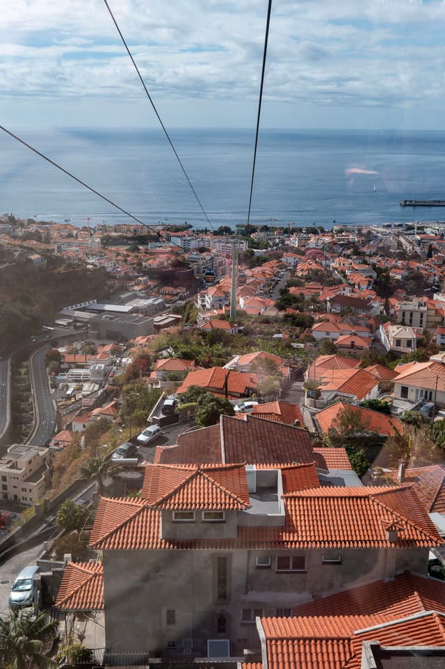 Aerial view of a coastal town with terra-cotta rooftops and a distant view of the ocean under a blue sky