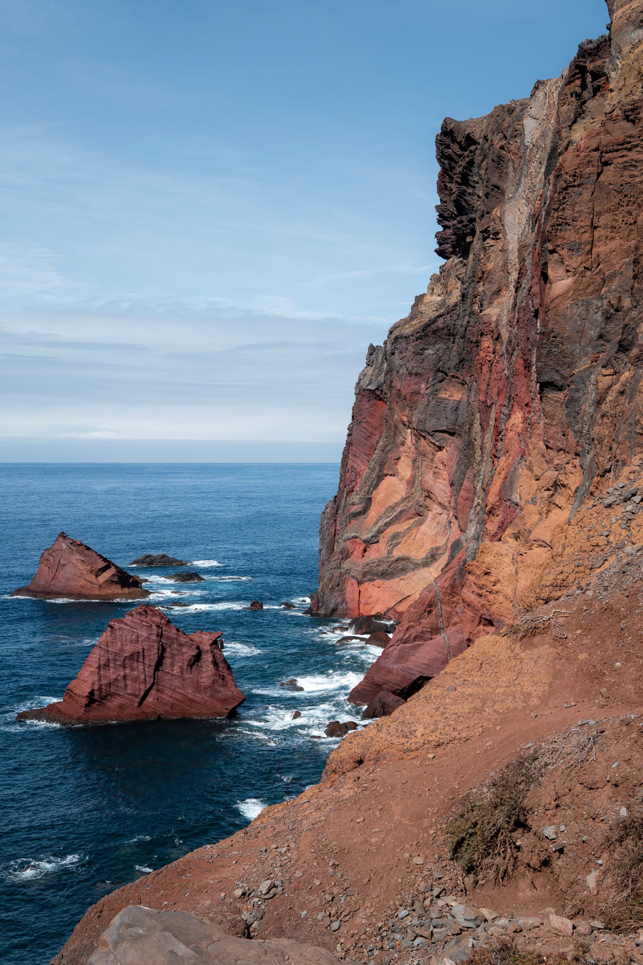 Rugged cliffs overlooking the ocean, with deep blue waters and waves crashing against rocky outcrops
