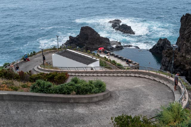 A winding road leads to a coastal area with a building, surrounded by rocky cliffs and the ocean