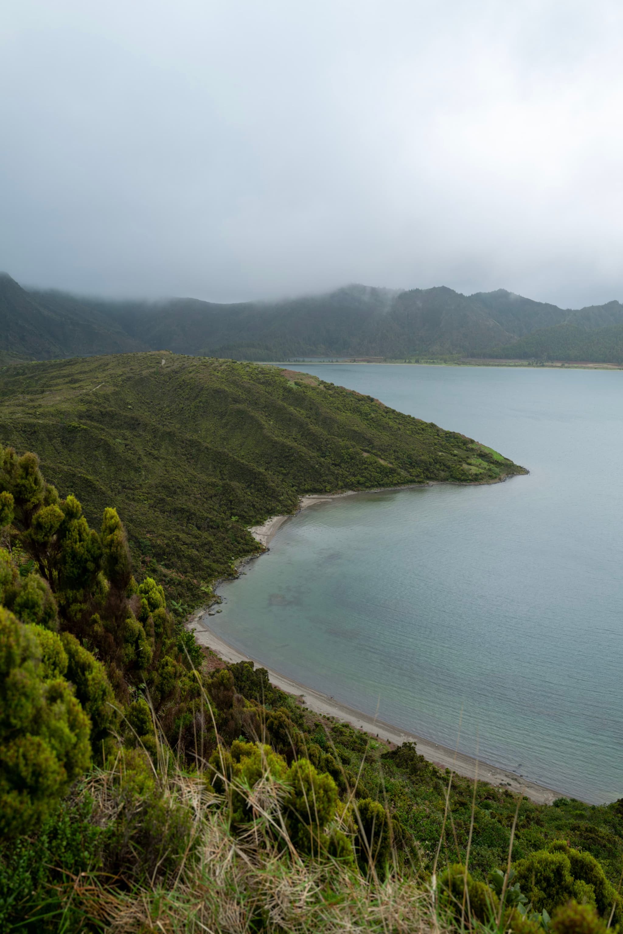 A serene coastal landscape with lush green hills, a calm body of water, and a cloudy sky
