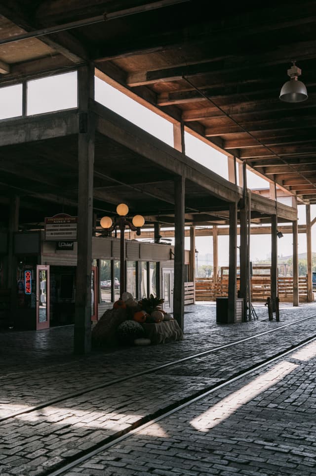 A rustic, open-air market with a wooden roof, cobblestone floor, and scattered light fixtures