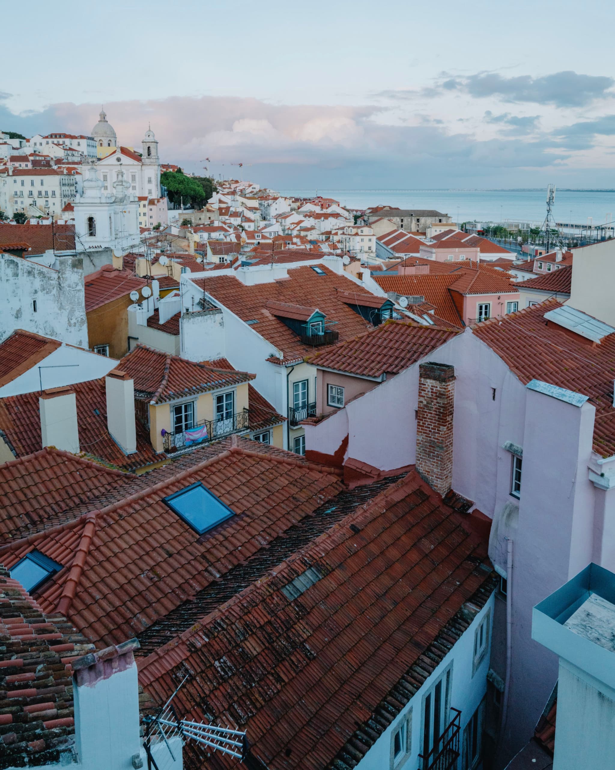 A scenic view of a coastal town with red-tiled rooftops, pastel-colored buildings, and a distant ocean horizon under a cloudy sky